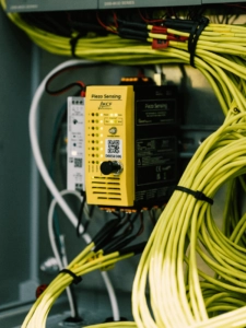 KCF Technologies piezo sensing monitor with yellow face and black side with yellow writing, surrounded by sensor wires neatly bundled for safety and cleanliness.