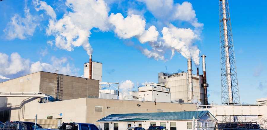 Large industrial plant in front of a blue sky with plumes of water vapor.