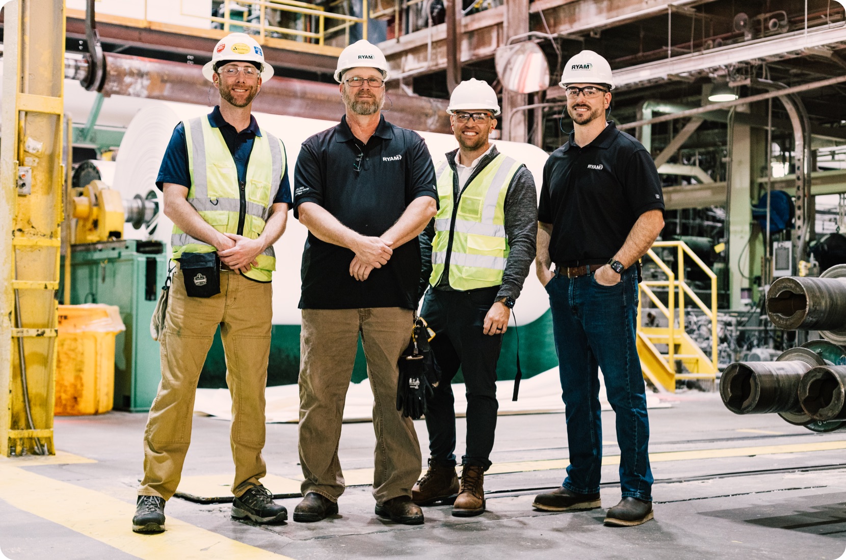 KCF Team, four men in hard hats, two in yellow vests and two in black shirts, smiles on an industrial site.