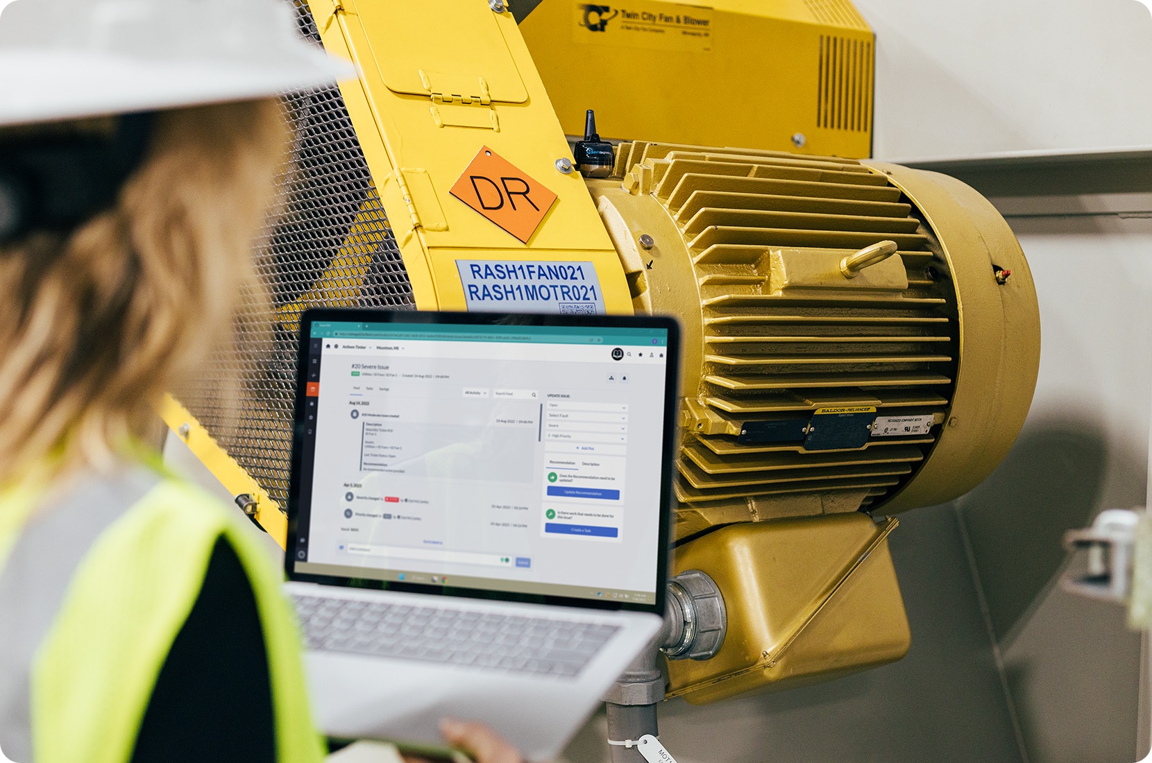 Technician monitors real time machine health data on a laptop in front of industrial machinery.