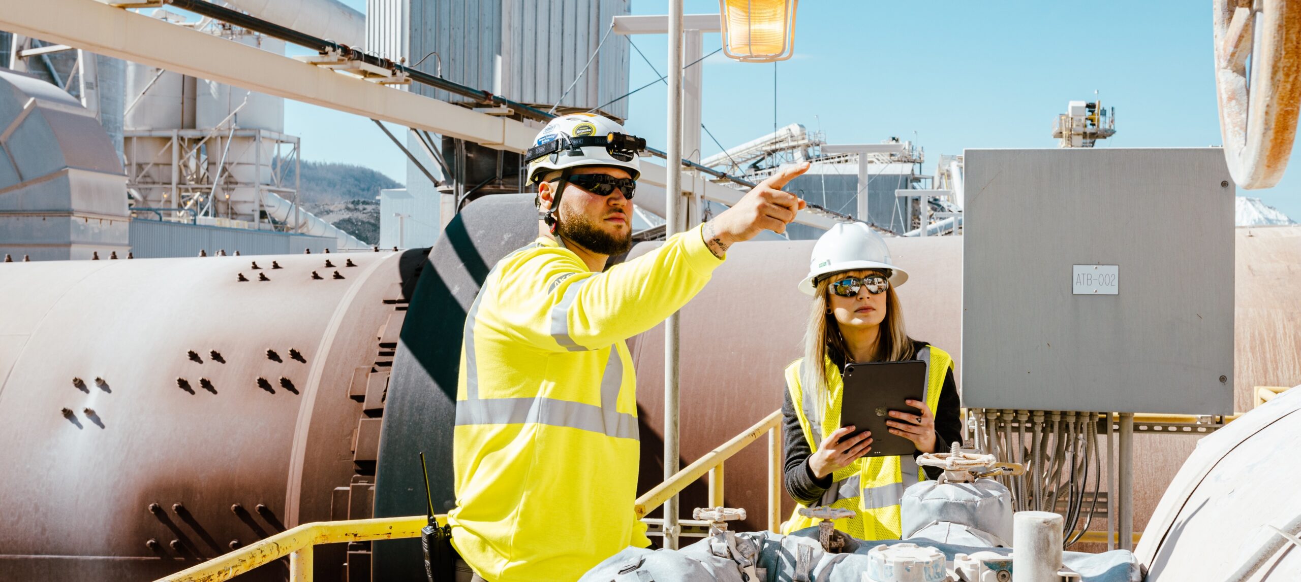 Two KCF engineers discuss solutions on site with a tablet in hand. Both are wearing hardhats and PPE.