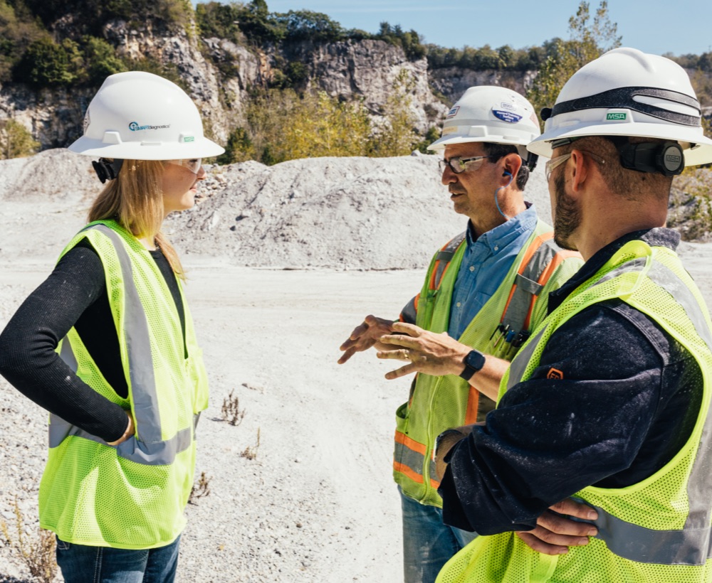 KCF team discusses solutions on site, wearing white hardhats and PPE.