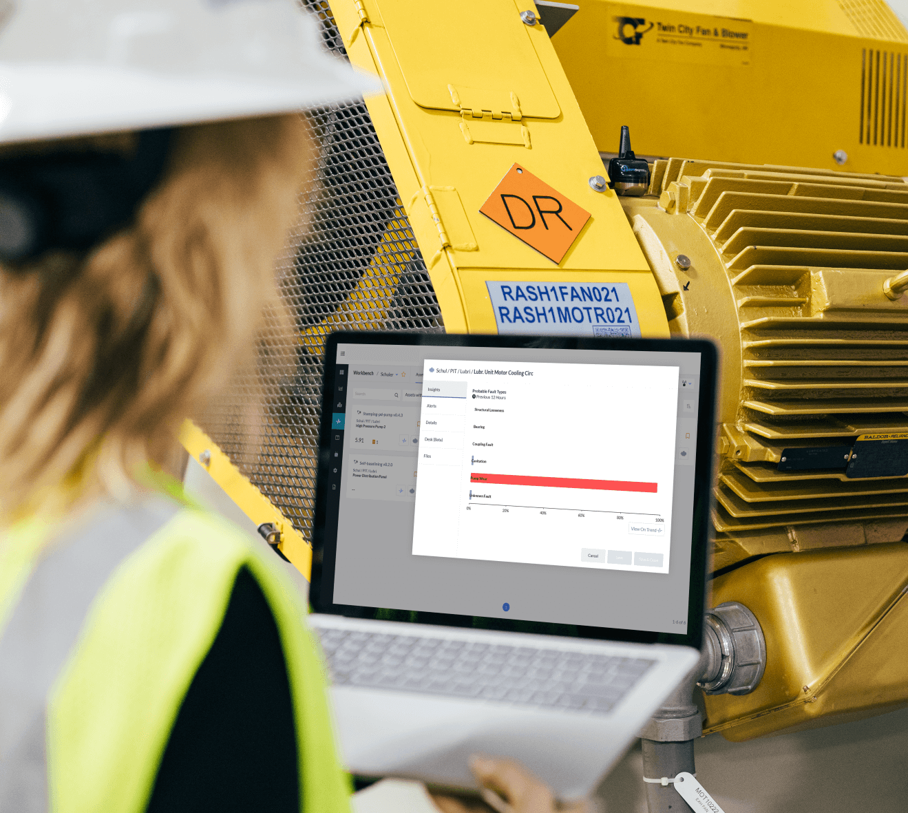 KCF Technician monitors machine health on their laptop in front of a yellow industrial machine.