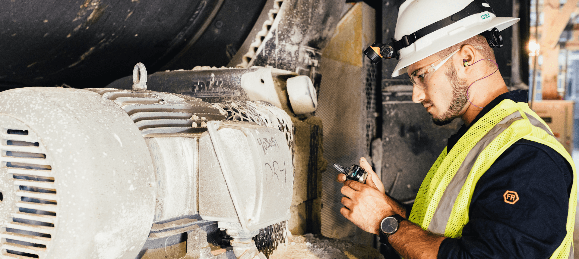 KCF Technician in a white hard hat and PPE places a vibration monitor on industrial machinery to monitor machine health.