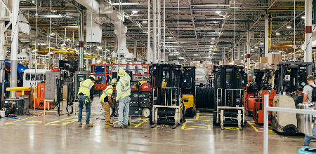 Warehouse or production floor with forklifts and scissors lifts lined up.