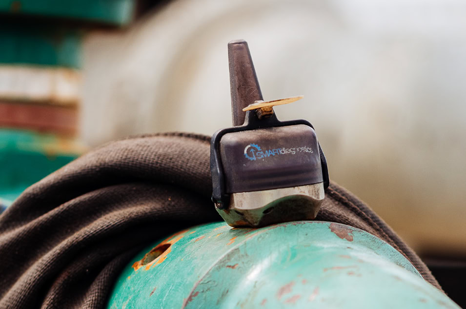 SMARTdiagnostics vibration monitor on teal green pipe in an oil and gas setting.